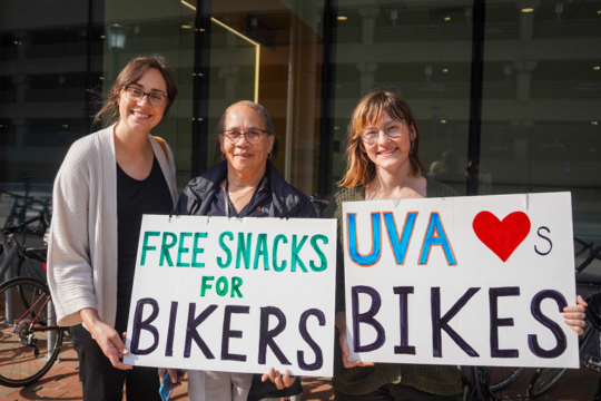 Outreach staff smiling with signs that say Free Snacks for Bikers and UVA Loves Bikes