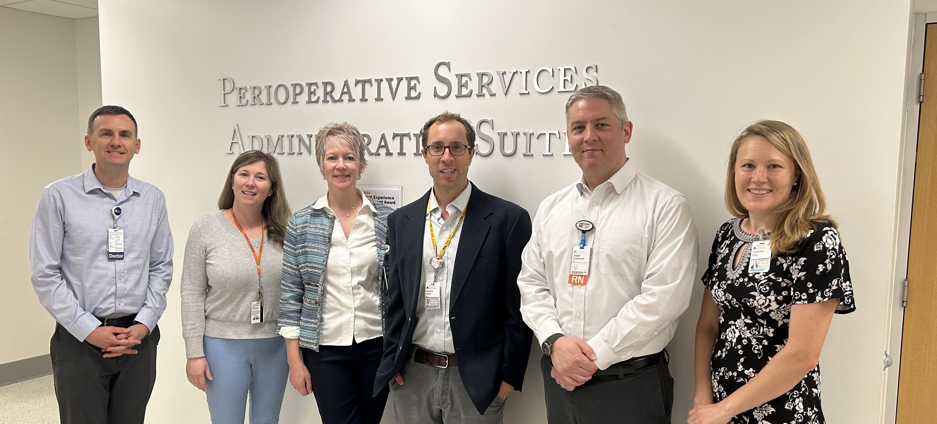 Five clinicians and one staff member posing in front of Perioperative Services Administrative Suite