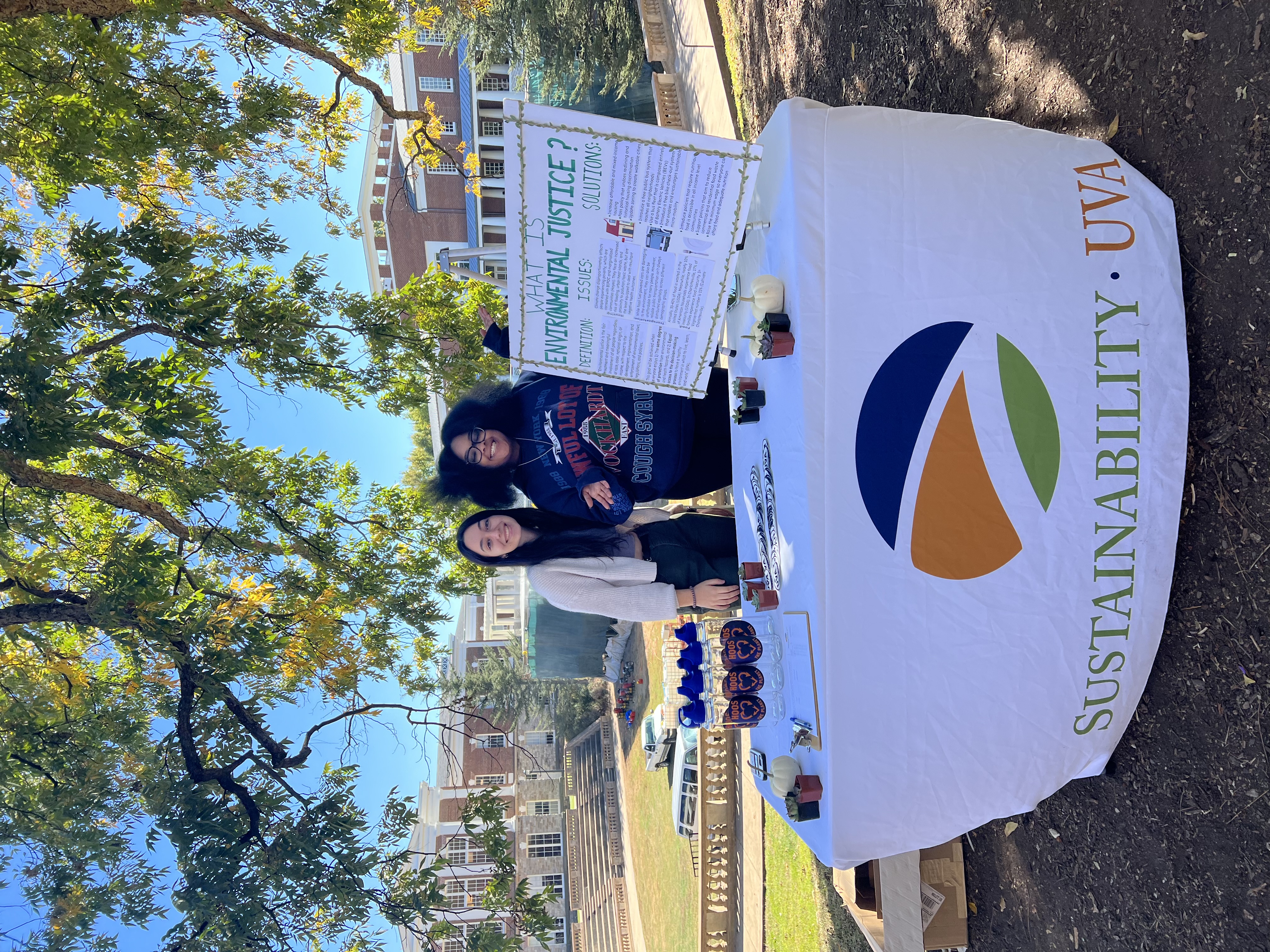 Two members of the Equity & Environment team stand behind a table with a poster that reads, "What is Environmental Justice?"