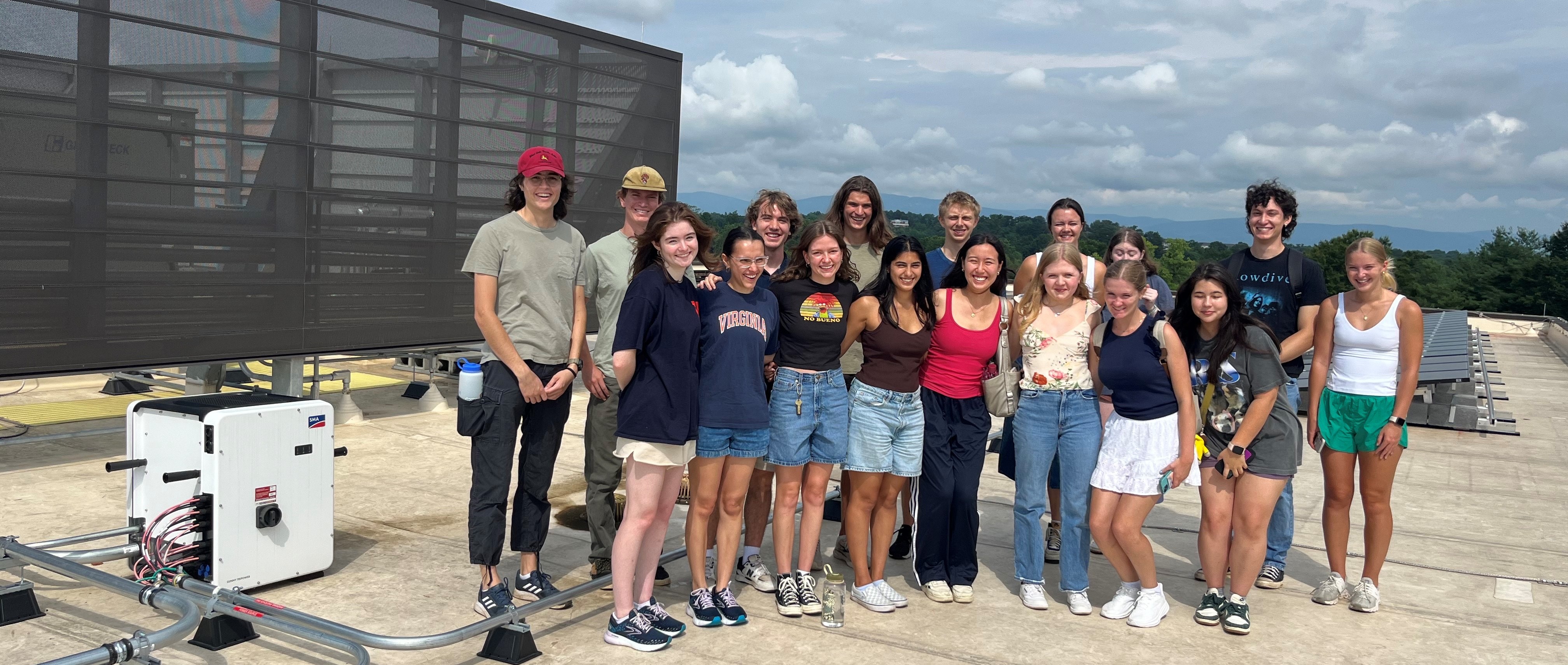 Students stand on a roof by solar panels while smiling