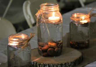 Mason Jars with a water and a candle floating inside on top of tree cutting as a decoration on a table