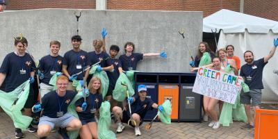 Students wearing navy sustainability t-shirts and carrying pickers and green compost bags gathered around a zero waste station in Scott Stadium. 