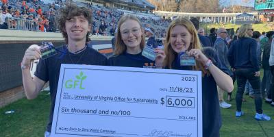 Three Office for Sustainability student employees holding a check on the field at Scott Stadium. 