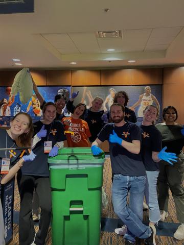 UVA Students pose and smile around a green compost bin in John Paul Jones Arena