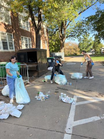 Three Zero Waste Ambassadors pose for a photo while sorting through compost outside Halsey Hall.
